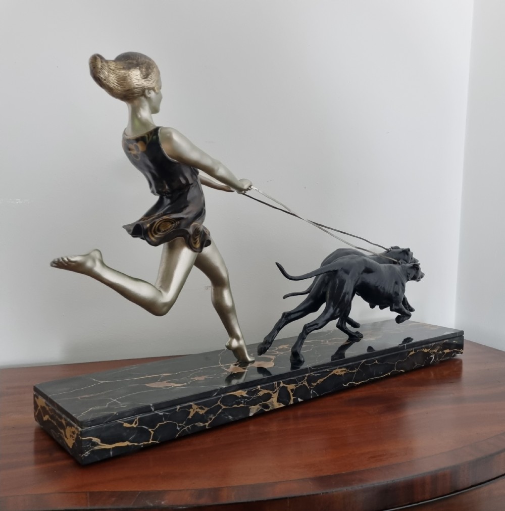 An Art Deco sculpture depicting a silvered female figure running alongside two dark greyhounds, mounted on a black marble base. View VIII