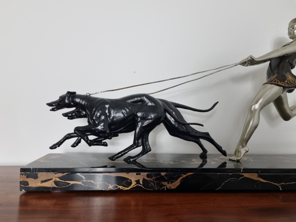 An Art Deco sculpture depicting a silvered female figure running alongside two dark greyhounds, mounted on a black marble base. View IX
