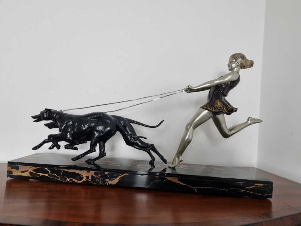An Art Deco sculpture depicting a silvered female figure running alongside two dark greyhounds, mounted on a black marble base. View X