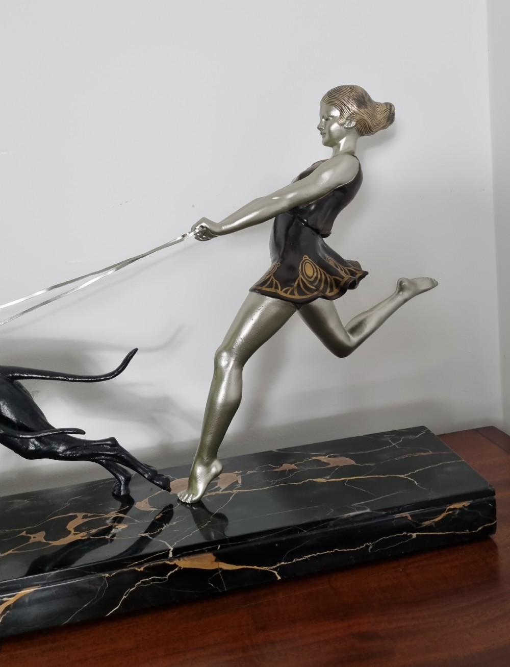An Art Deco sculpture depicting a silvered female figure running alongside two dark greyhounds, mounted on a black marble base. View XIV