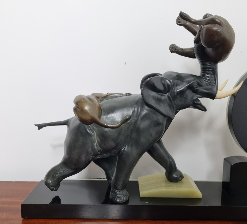 An Art Deco mantel clock featuring a circular green onyx dial flanked by dark patinated spelter sculptures of an elephant and panthers on a layered marble base. View II