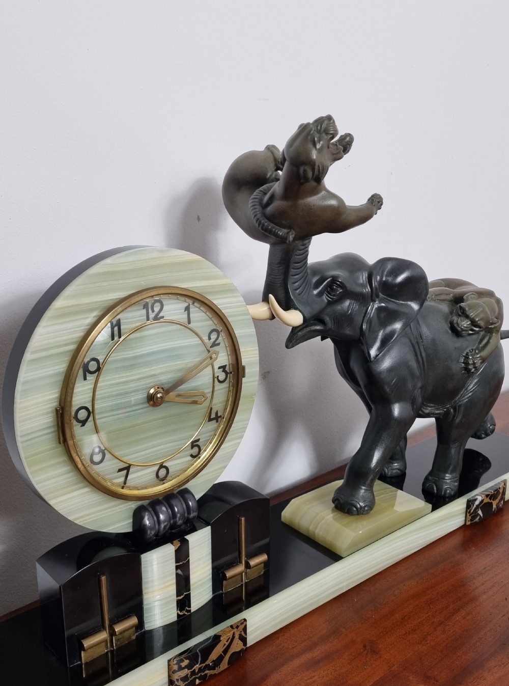 An Art Deco mantel clock featuring a circular green onyx dial flanked by dark patinated spelter sculptures of an elephant and panthers on a layered marble base. View VIII
