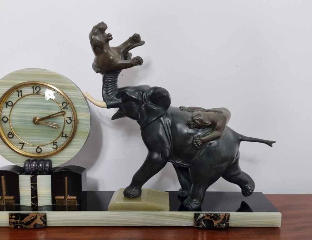 An Art Deco mantel clock featuring a circular green onyx dial flanked by dark patinated spelter sculptures of an elephant and panthers on a layered marble base. View XI