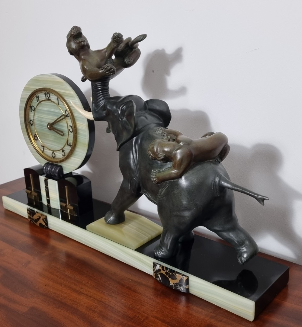 An Art Deco mantel clock featuring a circular green onyx dial flanked by dark patinated spelter sculptures of an elephant and panthers on a layered marble base. View XIII