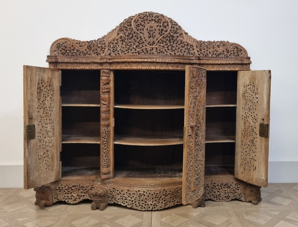 A 19th-century Anglo-Indian intricately carved teak wood cabinet featuring openwork floral lattice panels, figure pilasters, arched cresting, and carved animal feet. View III