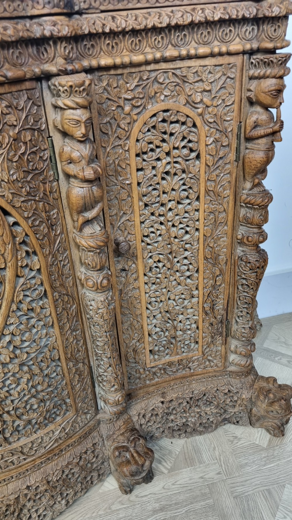 A 19th-century Anglo-Indian intricately carved teak wood cabinet featuring openwork floral lattice panels, figure pilasters, arched cresting, and carved animal feet. View XIII
