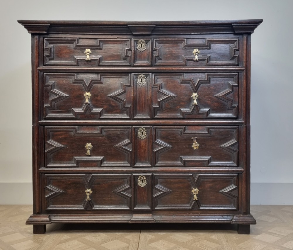 A seventeenth-century dark oak chest of four long drawers featuring geometric panel mouldings and brass teardrop handles. View II
