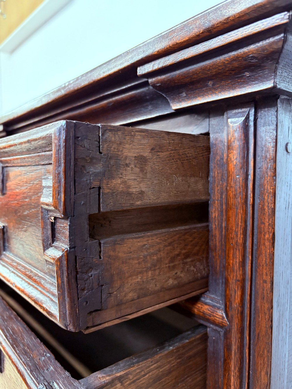 A seventeenth-century dark oak chest of four long drawers featuring geometric panel mouldings and brass teardrop handles. View VII