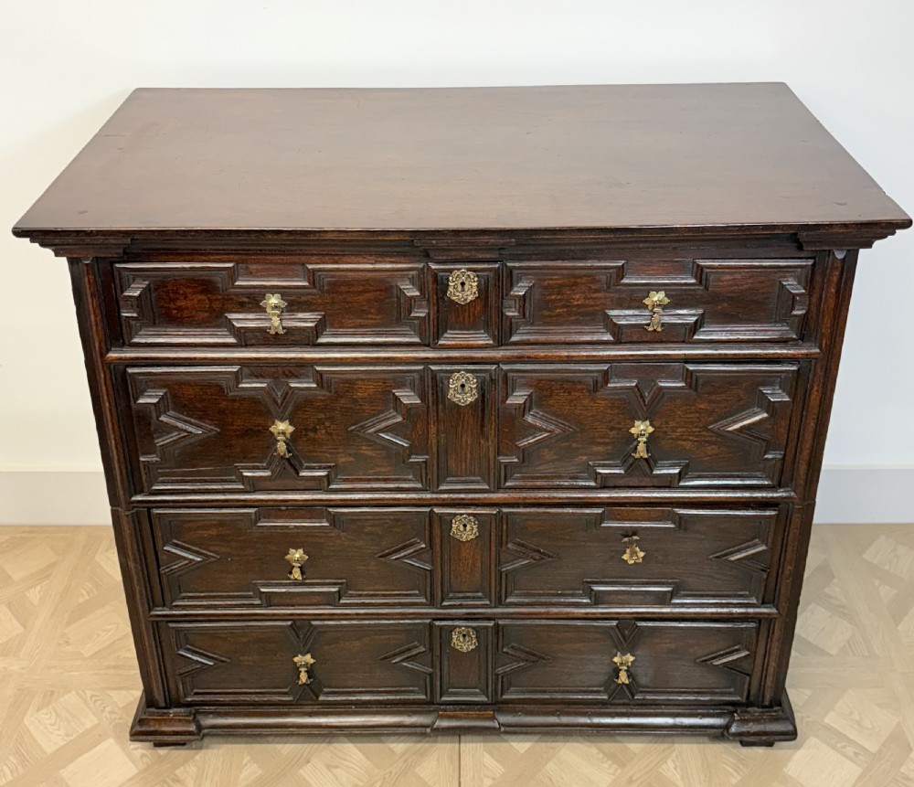 A seventeenth-century dark oak chest of four long drawers featuring geometric panel mouldings and brass teardrop handles. View IX