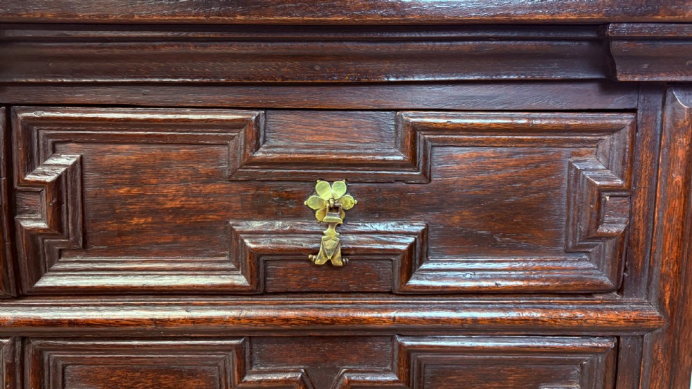 A seventeenth-century dark oak chest of four long drawers featuring geometric panel mouldings and brass teardrop handles. View X