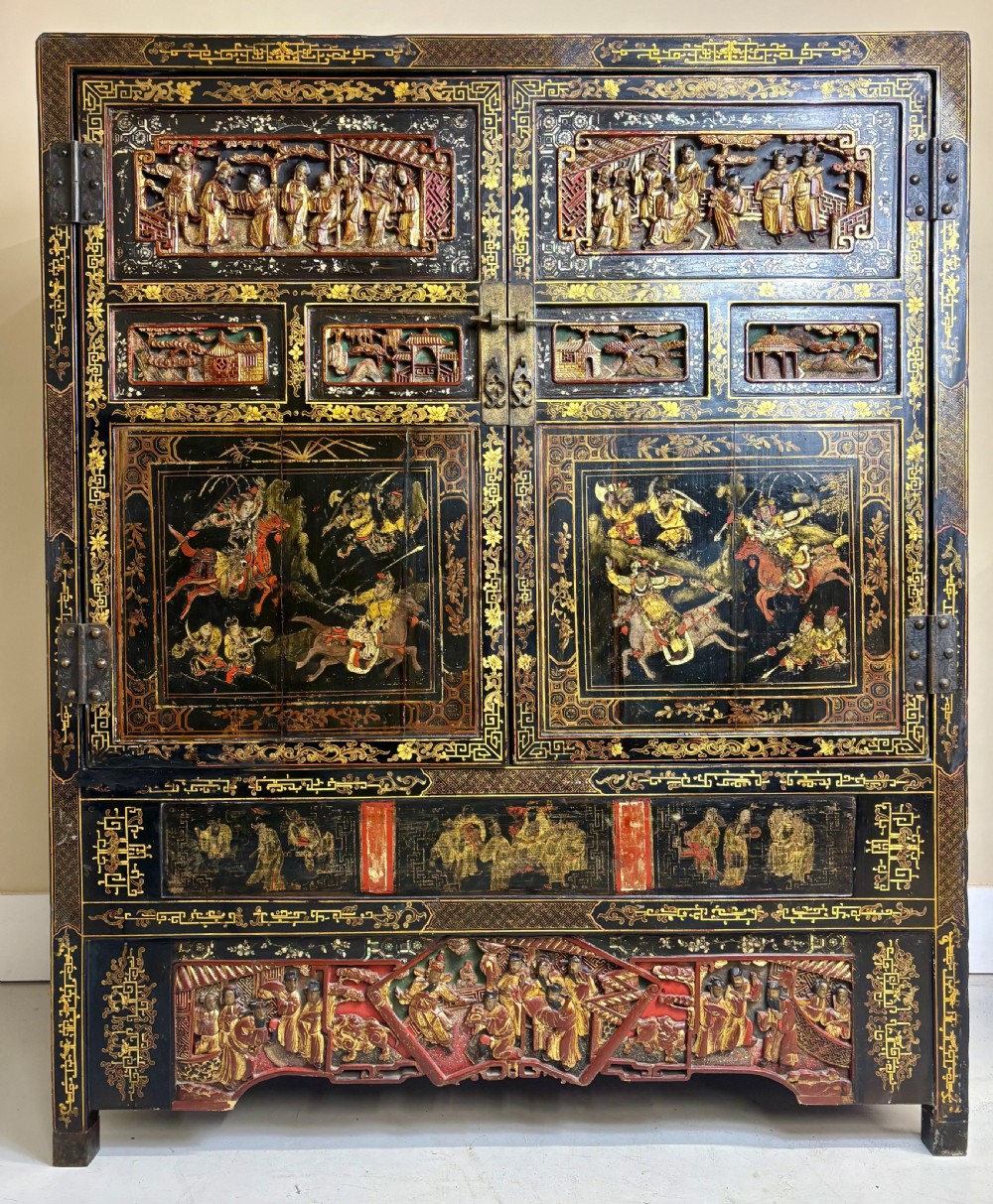 Late 19th-century Chinese black lacquer cabinet featuring intricate hand-carved polychrome figures, gilded panels of warriors on horseback, and brass door fittings. View VIII
