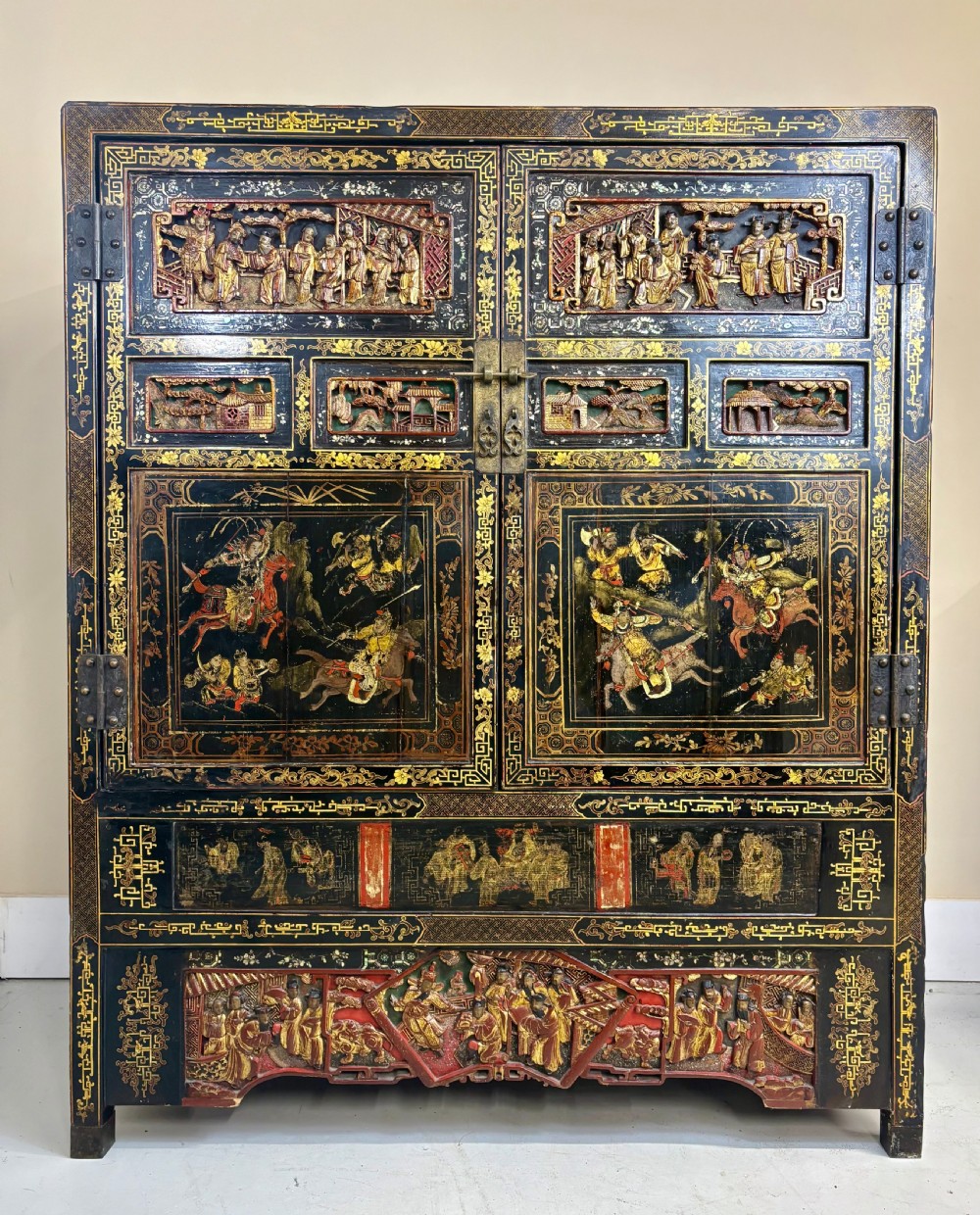 Late 19th-century Chinese black lacquer cabinet featuring intricate hand-carved polychrome figures, gilded panels of warriors on horseback, and brass door fittings. View II