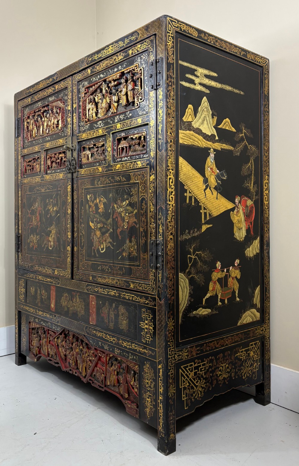 Late 19th-century Chinese black lacquer cabinet featuring intricate hand-carved polychrome figures, gilded panels of warriors on horseback, and brass door fittings. View IV
