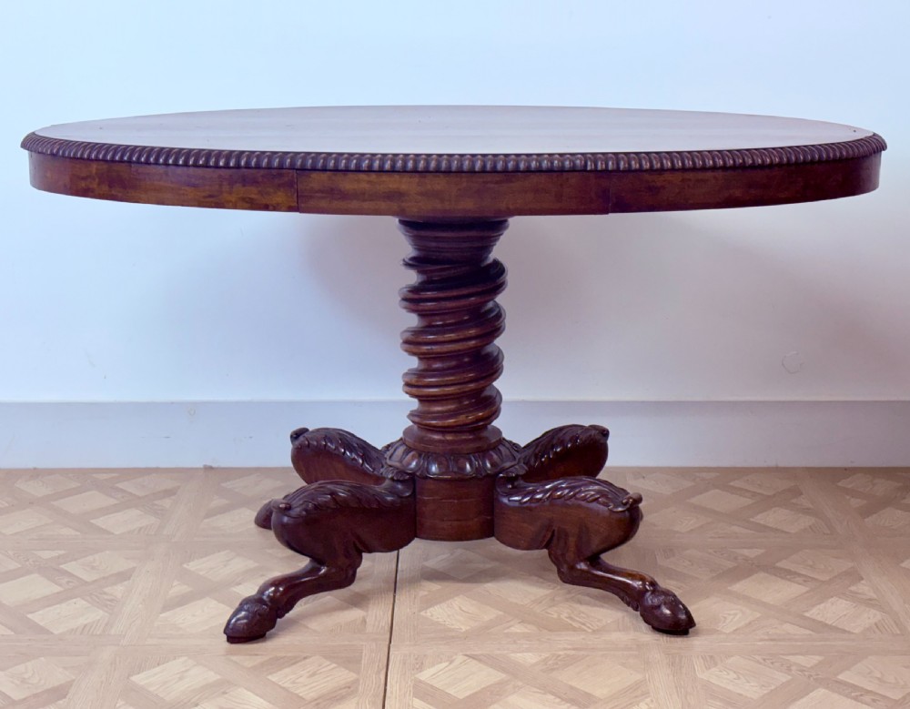A circular Regency burr walnut centre table featuring a carved spiral pedestal and a four-legged base with carved animal feet.