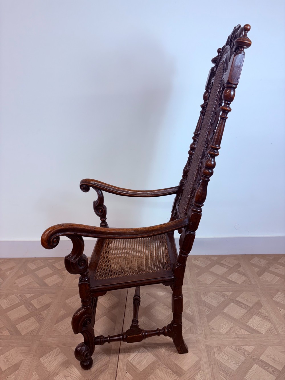 A late 17th-century Carolean dark walnut armchair featuring an intricately carved cresting rail, high caned back panel, curved arms, and turned legs. View II