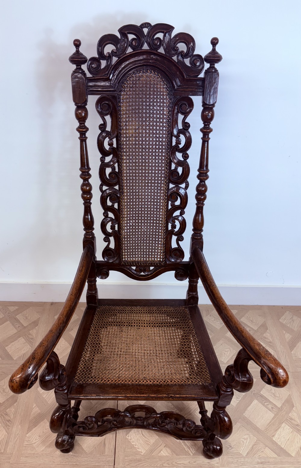 A late 17th-century Carolean dark walnut armchair featuring an intricately carved cresting rail, high caned back panel, curved arms, and turned legs. View V
