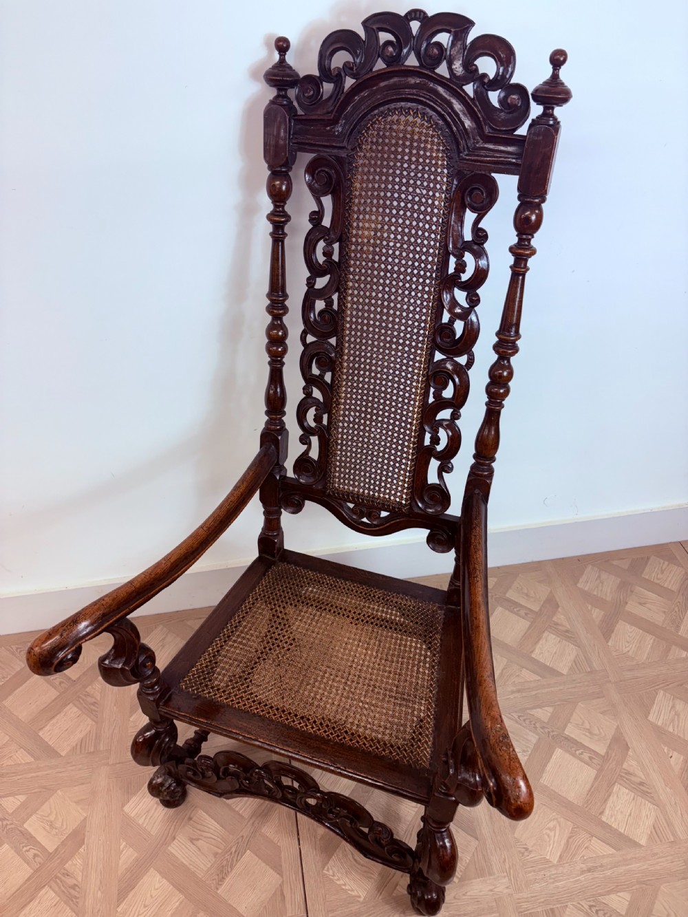 A late 17th-century Carolean dark walnut armchair featuring an intricately carved cresting rail, high caned back panel, curved arms, and turned legs. View VII