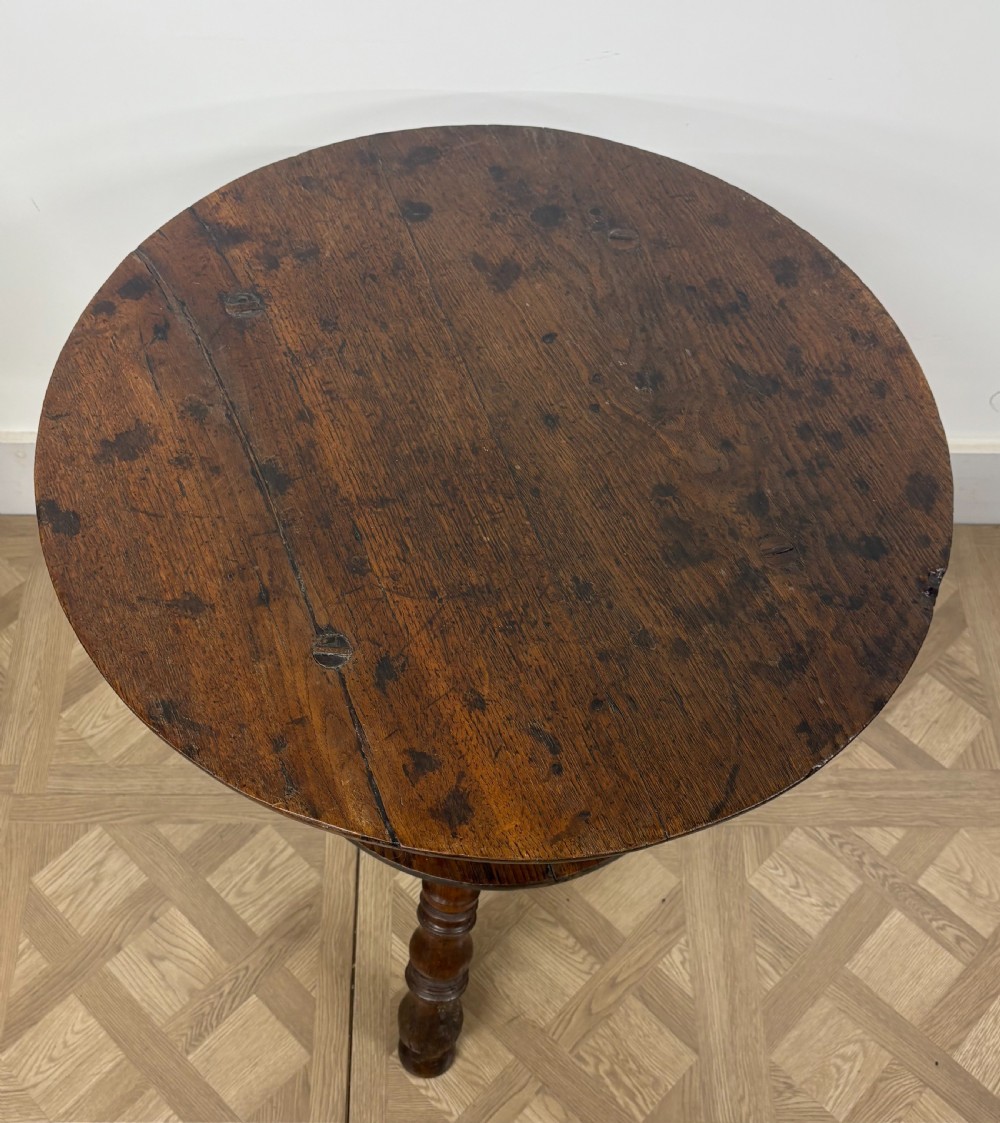 An 18th-century dark oak cricket table featuring a circular plank top, three turned legs, and an integrated lower circular shelf. View III