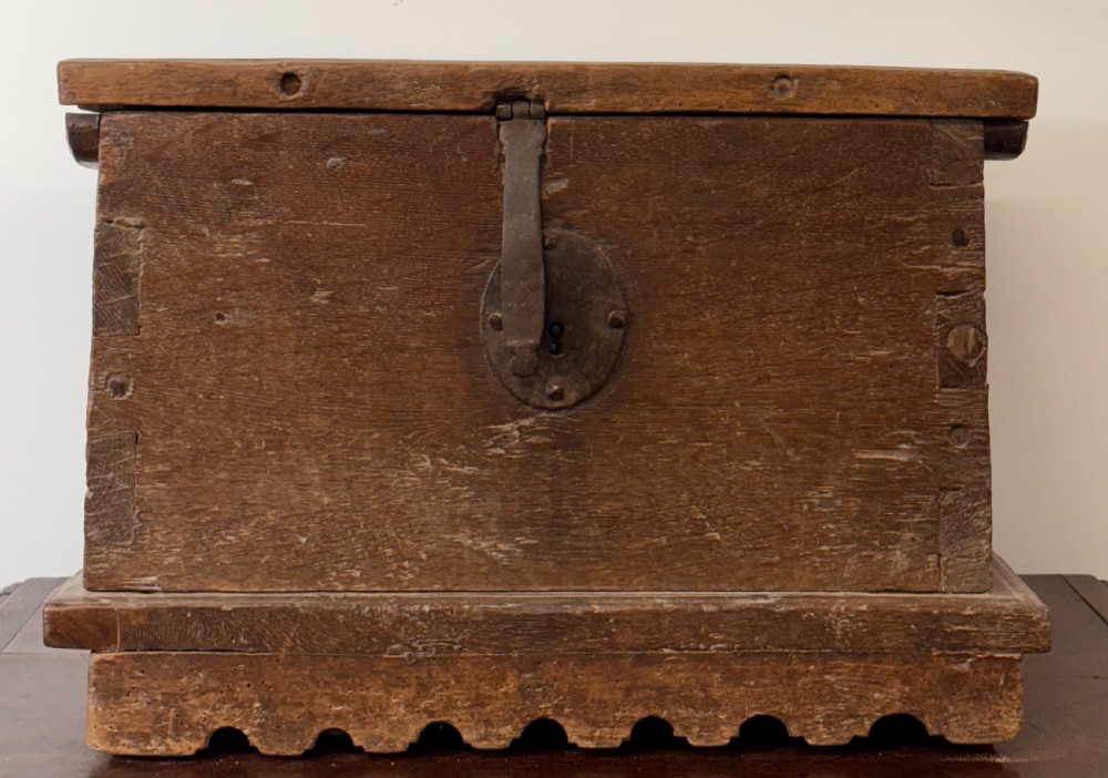 A late sixteenth to early seventeenth-century Flemish oak coffer featuring hand-forged iron clasp hardware, wooden pegs, and a scalloped base plinth.