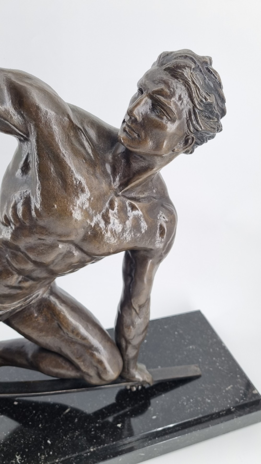 An Art Deco dark bronze sculpture depicting a muscular male athlete bending an iron bar, mounted on a black marble plinth. View VIII