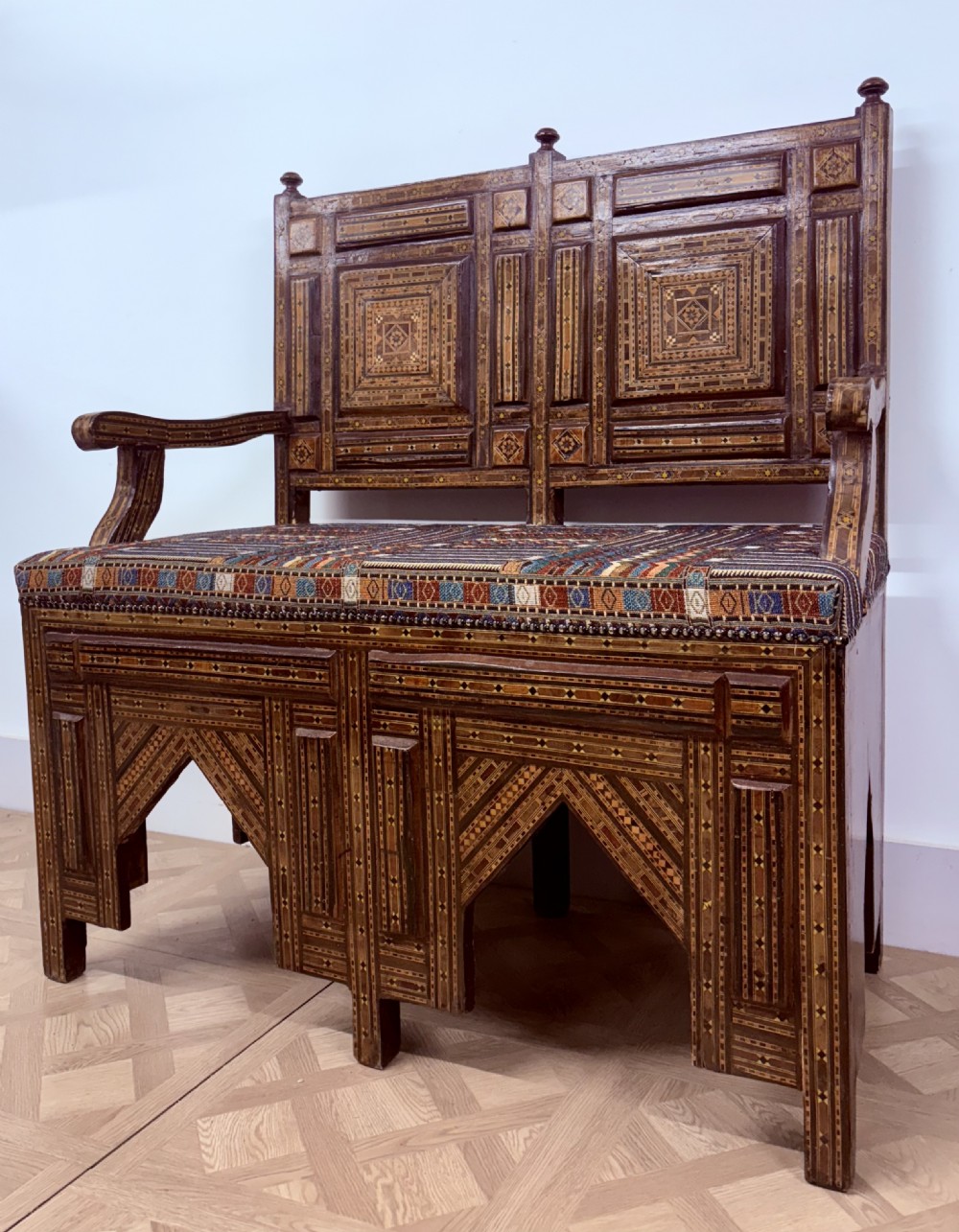 A 19th-century double-back Syrian hardwood bench featuring intricate geometric bone and timber parquetry inlay with a patterned upholstered seat. View VI