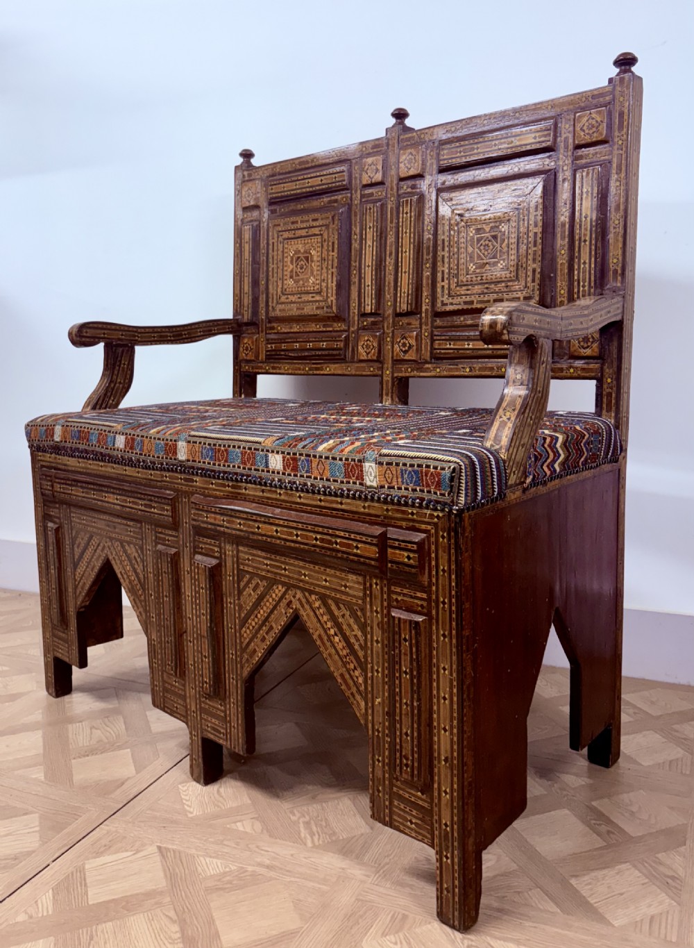 A 19th-century double-back Syrian hardwood bench featuring intricate geometric bone and timber parquetry inlay with a patterned upholstered seat. View VIII