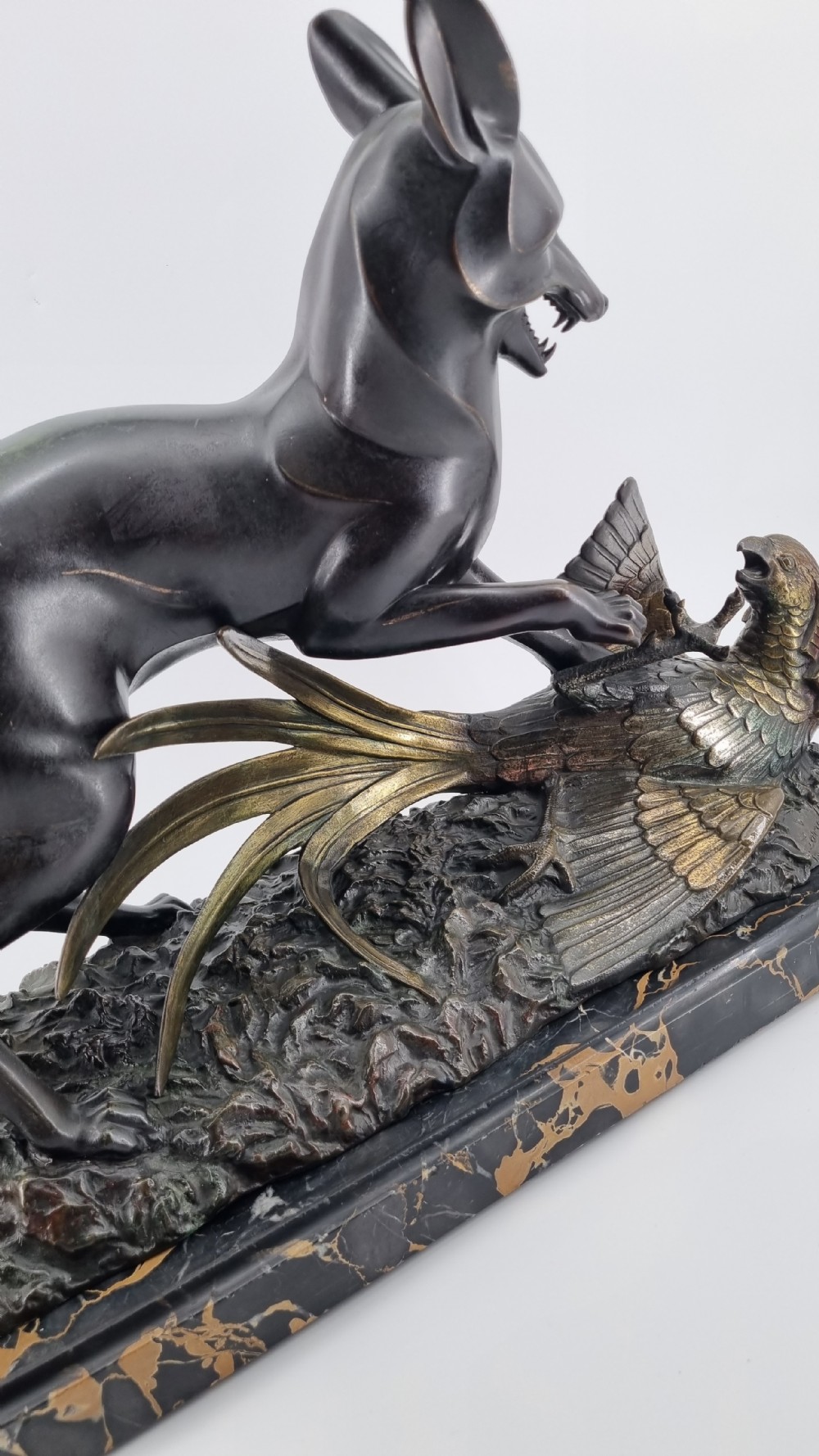 A dark patinated bronze sculpture depicting a fox capturing a pheasant mounted on a black veined marble base. View V