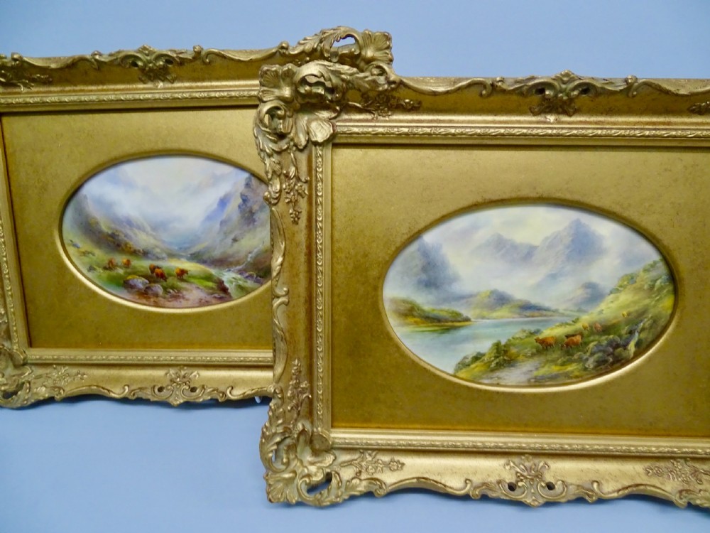 A pair of gilt-framed oval porcelain plaques featuring hand-painted highland landscape scenes with cattle.