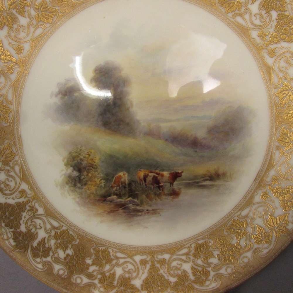 A pair of round Royal Worcester porcelain cabinet plates featuring hand-painted scenes of cattle in landscapes, bordered by ornate gold scrollwork gilding on a cream ground. View II