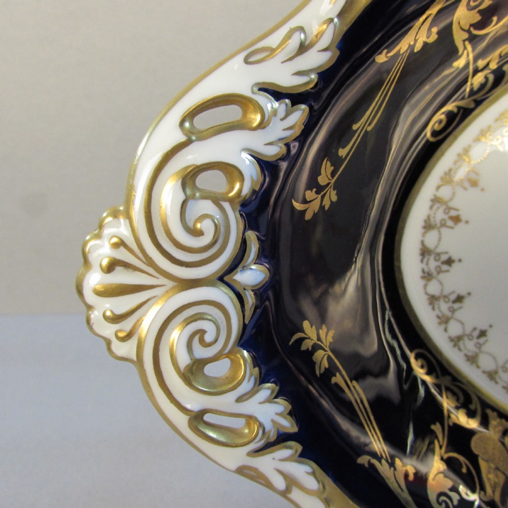 An oval porcelain dish featuring a cobalt blue border, gold scroll decoration, pierced handles, and a central hand-painted floral bouquet reserve. View II