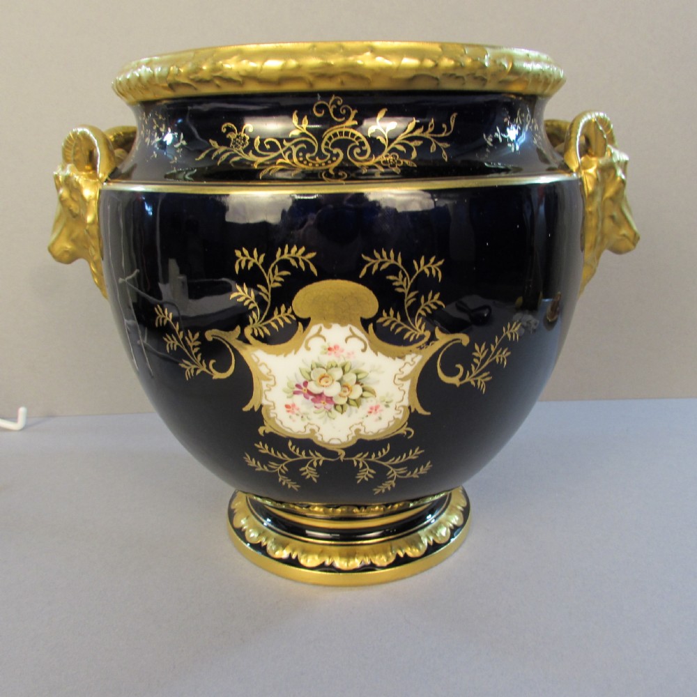 A cobalt blue porcelain jardiniere featuring gilded ram head handles, elaborate scroll gilding, and a central painted vignette of birds. View III