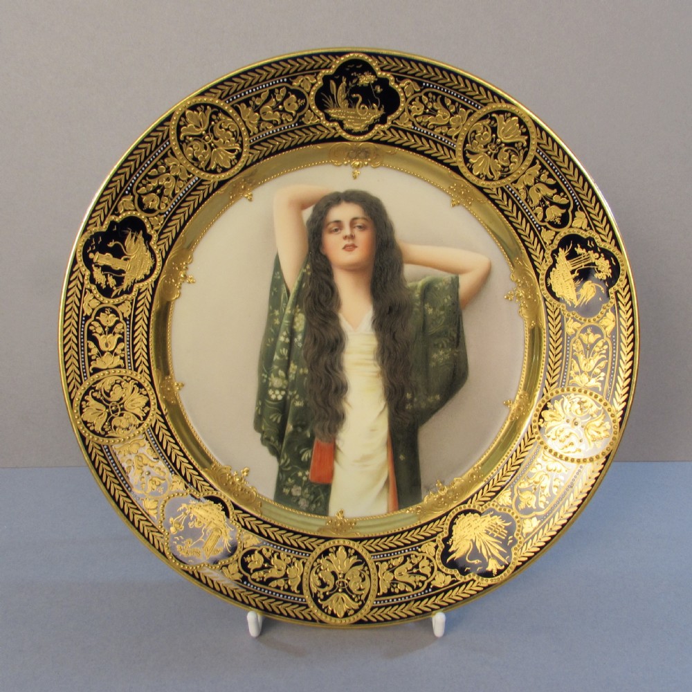 A circular Vienna porcelain cabinet plate featuring a central hand-painted portrait of a woman with long dark hair surrounded by an elaborate gilded and dark border.