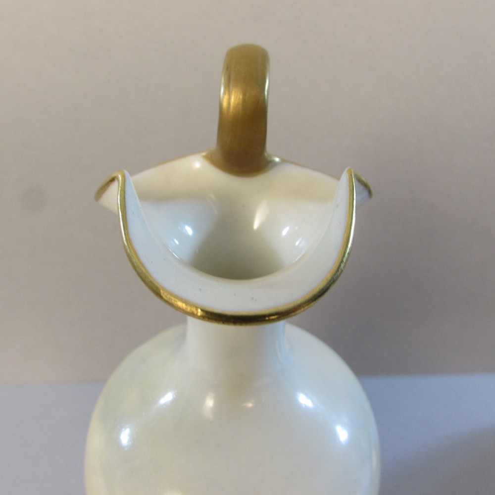 An ornate porcelain ewer featuring a hand-painted scene of Highland cattle, a flared spout, a gilded scroll handle, and a square gold-finished base. View IV
