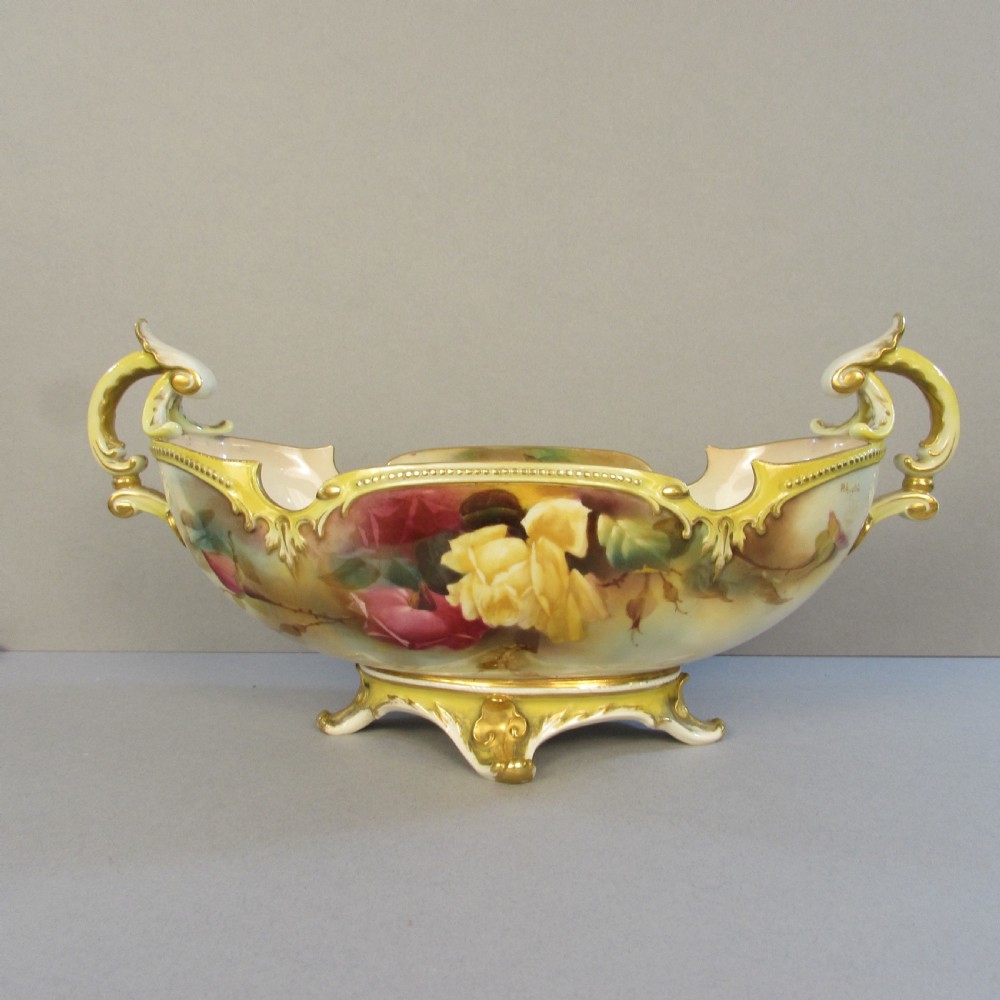 A hand-painted Royal Worcester porcelain centrepiece bowl featuring yellow and red roses, scroll handles, and gilt detailing on a footed base.