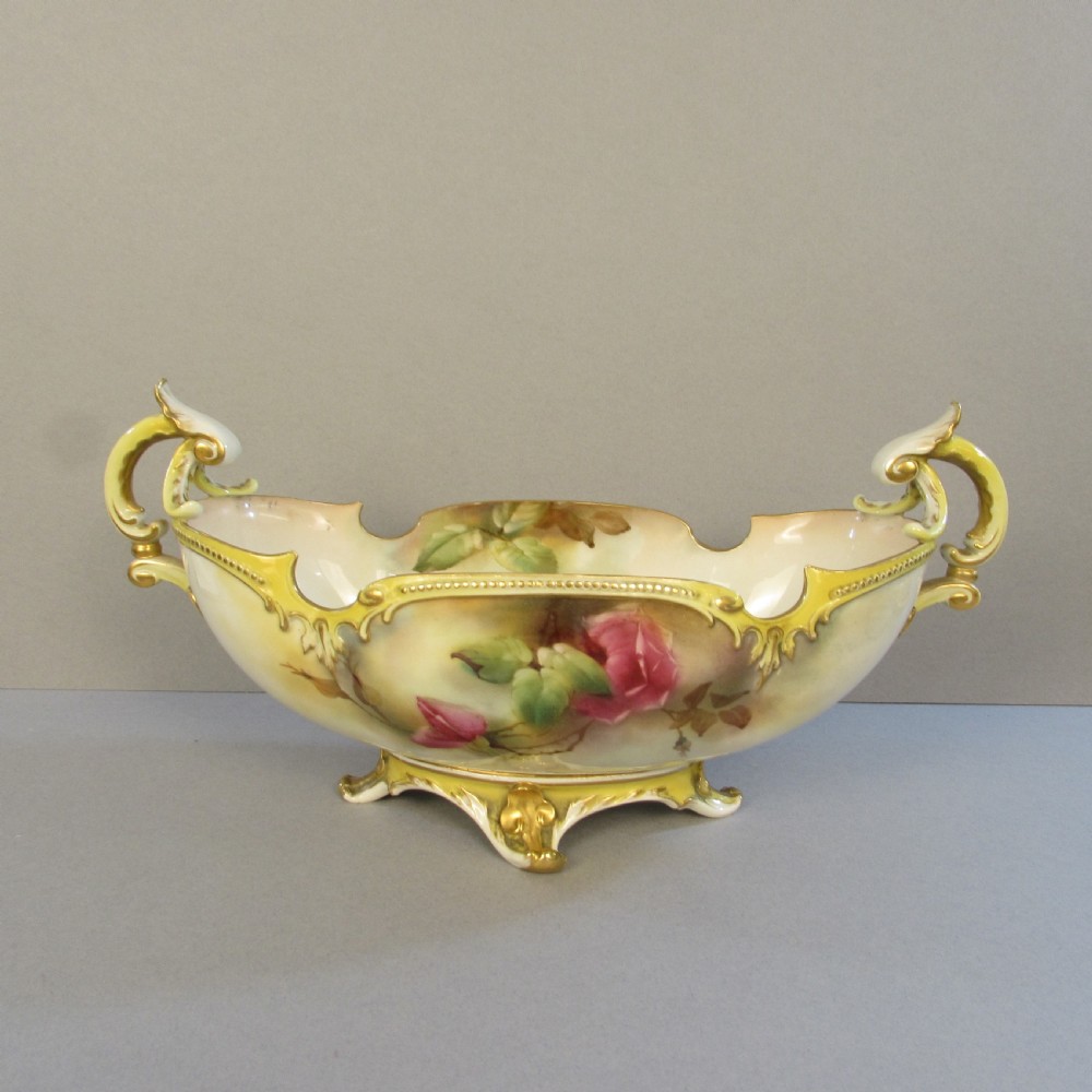 A hand-painted Royal Worcester porcelain centrepiece bowl featuring yellow and red roses, scroll handles, and gilt detailing on a footed base. View II