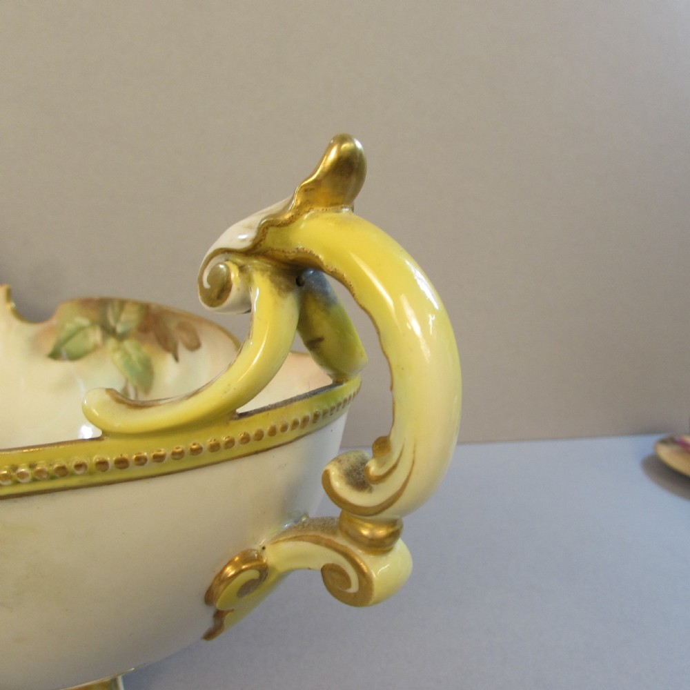 A hand-painted Royal Worcester porcelain centrepiece bowl featuring yellow and red roses, scroll handles, and gilt detailing on a footed base. View IV