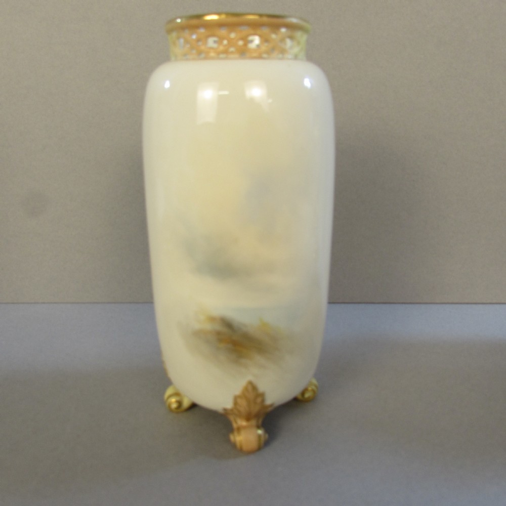 A cylindrical soft cream porcelain vase decorated with a painted scene of Highland sheep, featuring a reticulated gilt rim and four gilded scroll feet. View II