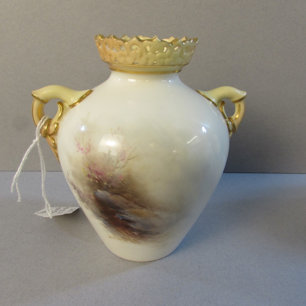 A cream porcelain vase with reticulated gilt rim, twin handles, and a hand-painted scene depicting Highland cattle in a misty landscape. View II
