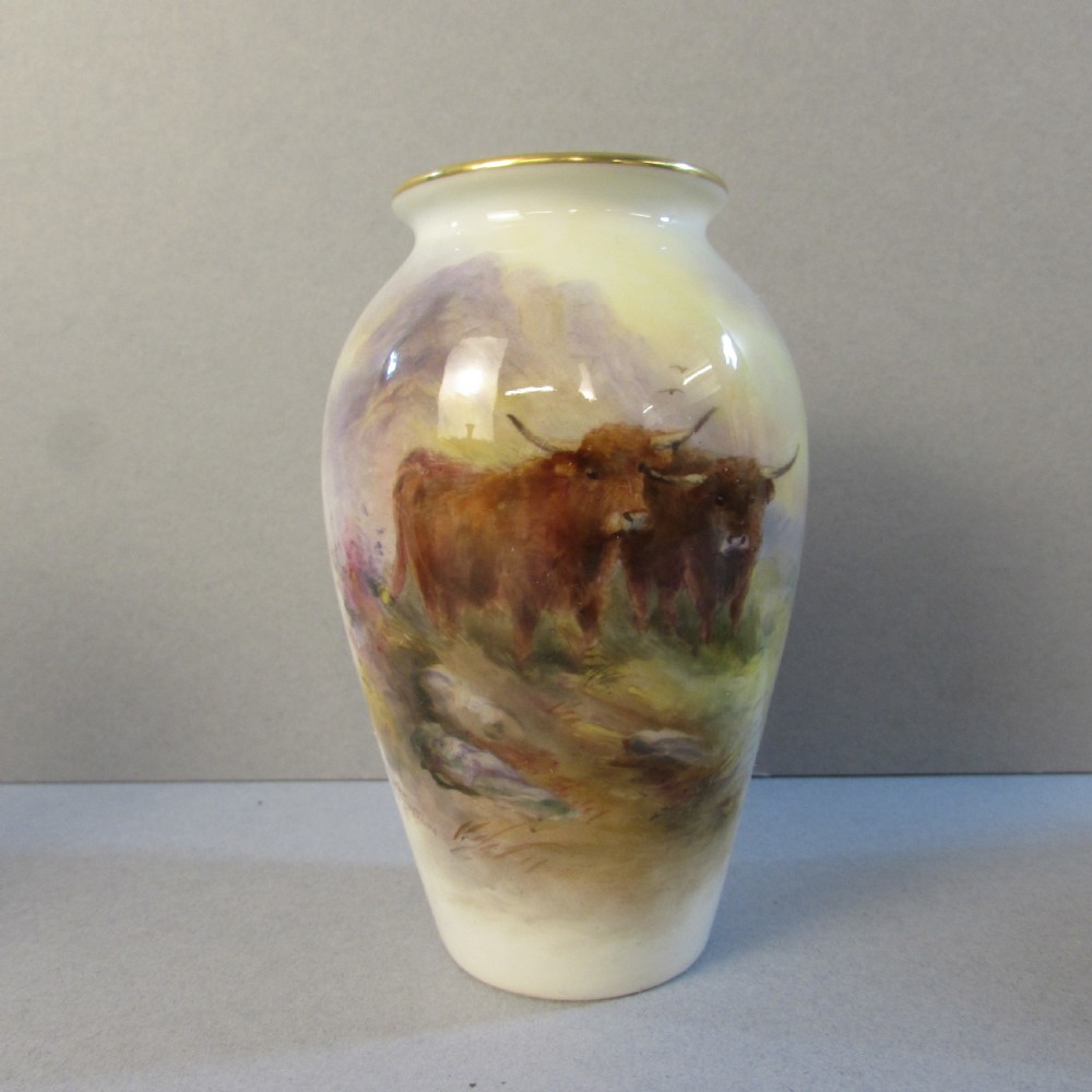 A cream baluster-shaped porcelain vase hand-painted with Highland cattle in a misty mountain landscape and finished with a gilt rim.
