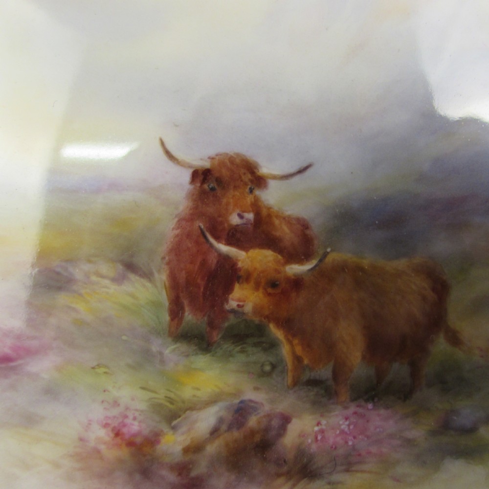 A pair of round antique Royal Worcester porcelain cabinet plates featuring hand-painted Highland cattle landscape scenes encircled by elaborate gilded cobalt blue borders. View V