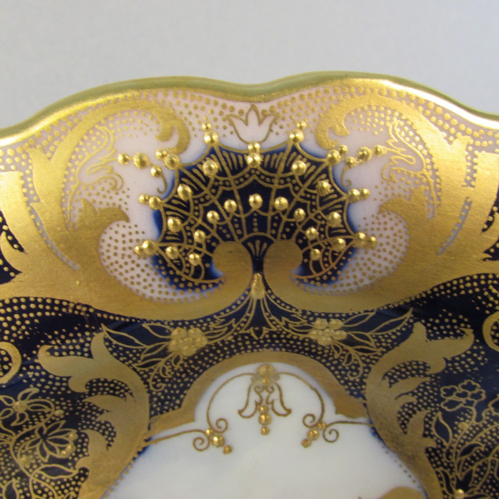 A pair of round antique Royal Worcester porcelain cabinet plates featuring hand-painted Highland cattle landscape scenes encircled by elaborate gilded cobalt blue borders. View VI