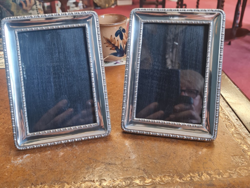 A pair of matching rectangular antique silver photo frames featuring double beaded borders standing upright.