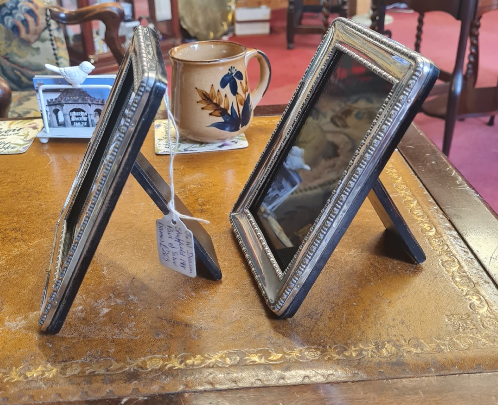 A pair of matching rectangular antique silver photo frames featuring double beaded borders standing upright. View IV