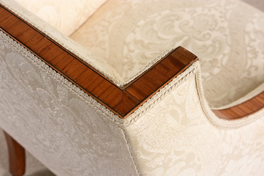 An antique three-piece Edwardian seating suite comprising a two-seater sofa and two matching armchairs upholstered in cream damask with mahogany frames and brass castors. View II