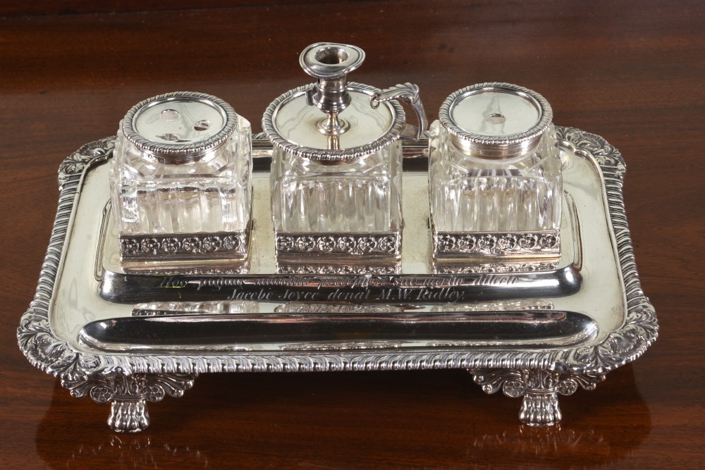 An Edwardian sterling silver desk stand with two cut-glass inkwells, a central chamber stick, and an engraved pen tray resting on paw feet.
