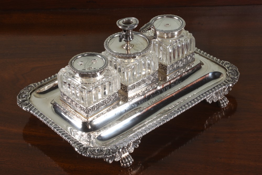 An Edwardian sterling silver desk stand with two cut-glass inkwells, a central chamber stick, and an engraved pen tray resting on paw feet. View II