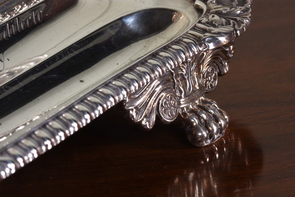 An Edwardian sterling silver desk stand with two cut-glass inkwells, a central chamber stick, and an engraved pen tray resting on paw feet. View VI