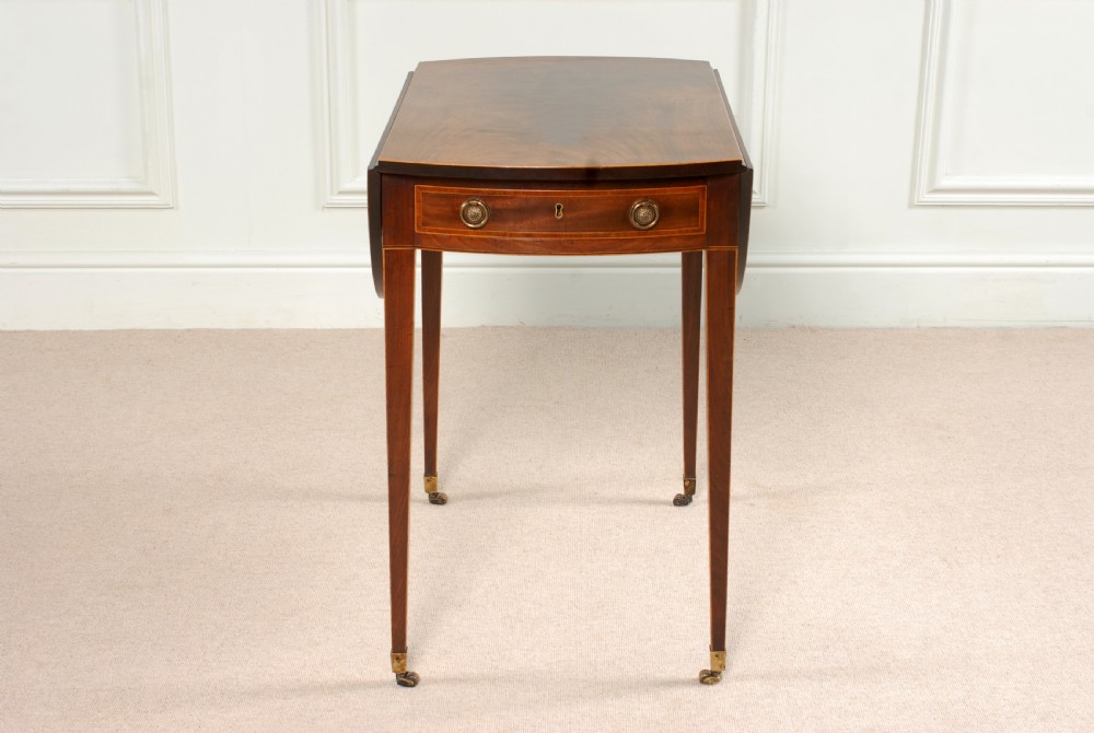 A Georgian Sheraton period mahogany oval Pembroke table with drop leaves, a single frieze drawer, boxwood inlay, and tapered legs ending in brass castors. View II