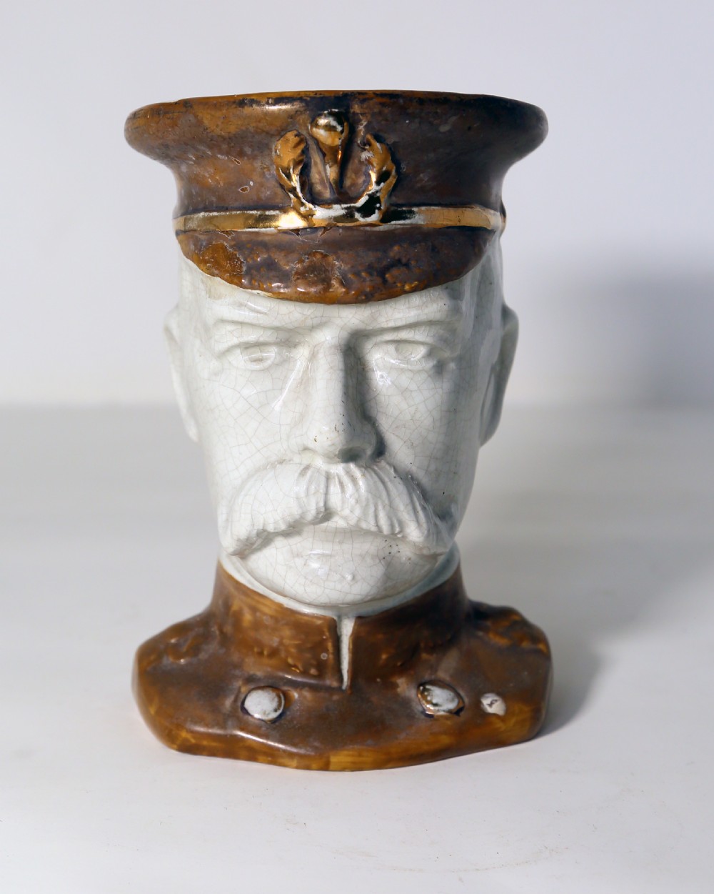 A glazed earthenware character jug formed in the shape of Lord Kitchener wearing a brown military peaked cap and uniform collar. View II