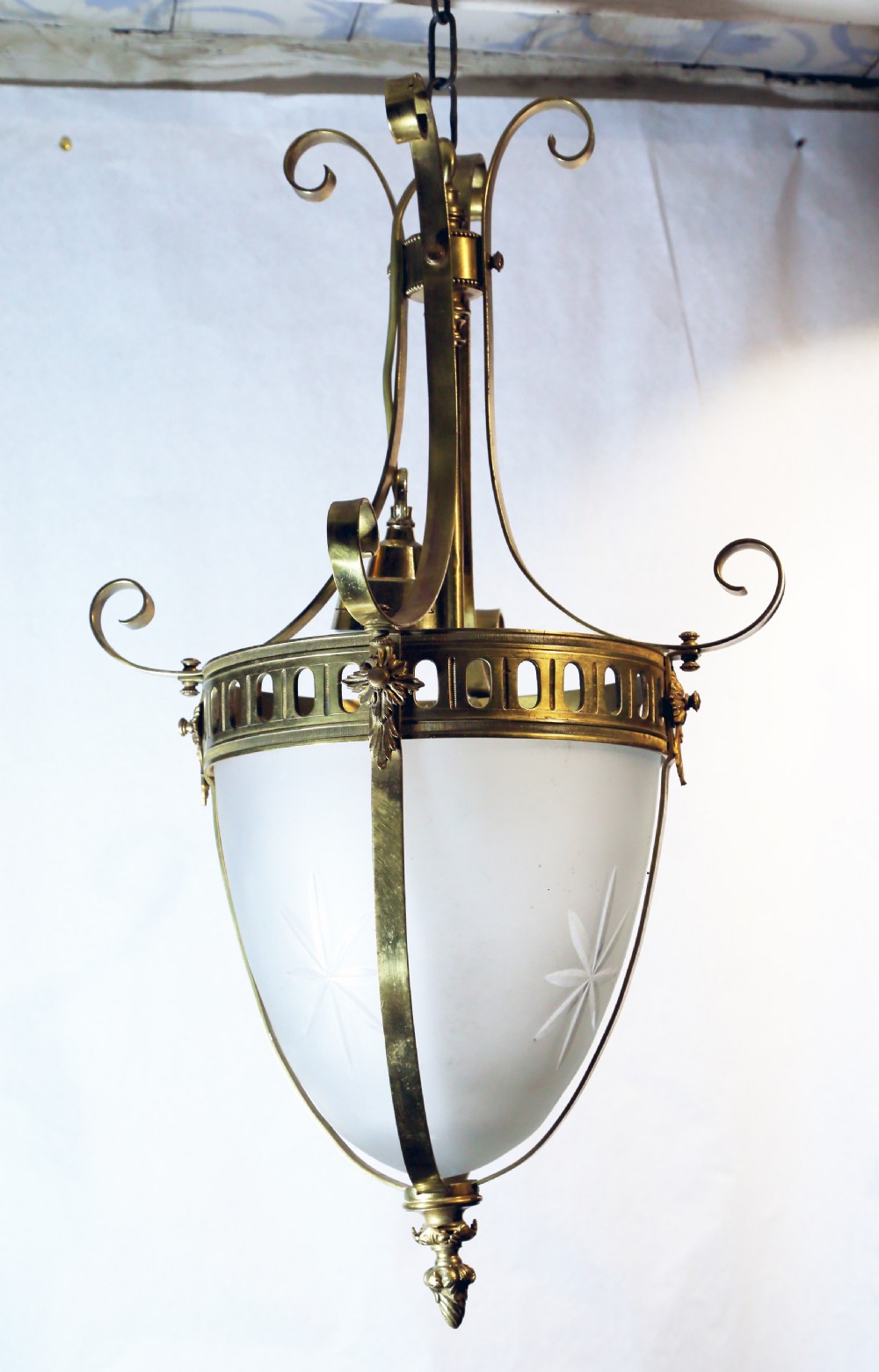 An Edwardian brass pendant lantern featuring a frosted glass shade decorated with etched star motifs and supported by scrolled brass straps.